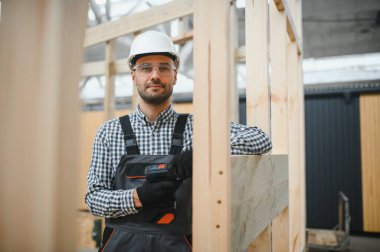 Modüler evlerin inşaat alanında miğfer takmış genç bir marangoz portresi..