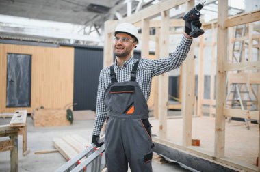 Modüler evlerin inşaat alanında miğfer takmış genç bir marangoz portresi..