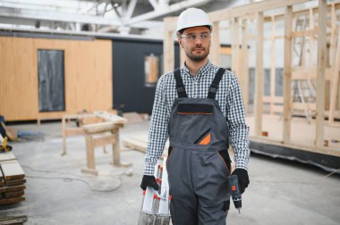 Modüler evlerin inşaat alanında miğfer takmış genç bir marangoz portresi..