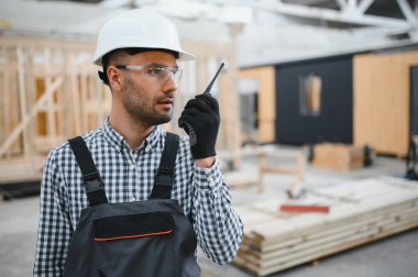 Bir mühendis modüler evlerin üretimini kontrol ediyor ve bir telsiz kullanıyor..