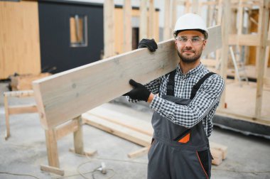 Modüler evlerin inşaat alanında miğfer takmış genç bir marangoz portresi..