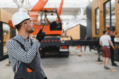 Foreman telsiz kullanarak prefabrik modüler bir evi kamyondan kamyona yüklüyor..