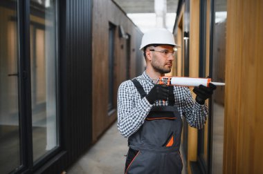 Bir işçi prefabrik modüler evdeki kuşak ve pencere çerçevesi arasındaki boşluğu doldurmak için poliüretan köpük uyguluyor..