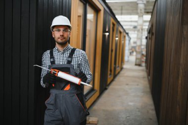 Bir işçi prefabrik modüler evdeki kuşak ve pencere çerçevesi arasındaki boşluğu doldurmak için poliüretan köpük uyguluyor..