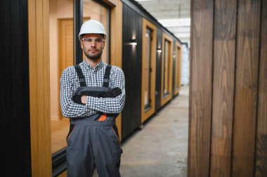 Modüler evlerin inşaat alanında miğfer takmış genç bir marangoz portresi..