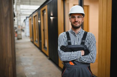 Modüler evlerin inşaat alanında miğfer takmış genç bir marangoz portresi..