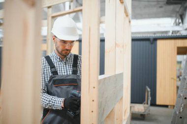 Modüler evlerin inşaat alanında miğfer takmış genç bir marangoz portresi..