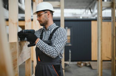 Modüler evlerin inşaat alanında miğfer takmış genç bir marangoz portresi..