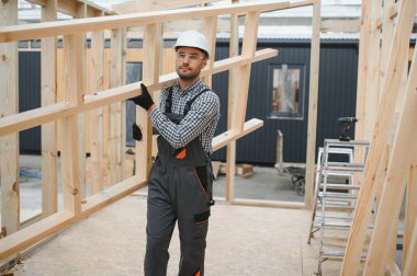 Modüler evlerin inşaat alanında miğfer takmış genç bir marangoz portresi..