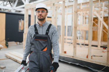 Modüler evlerin inşaat alanında miğfer takmış genç bir marangoz portresi..