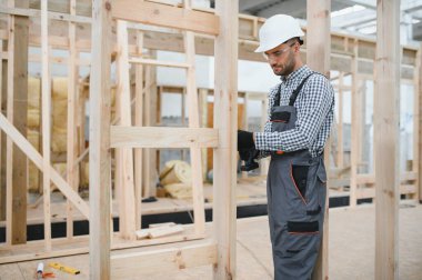 Üniformalı bir işçi ya da mühendis ahşap modüler evler için inşaat alanında çalışıyor..