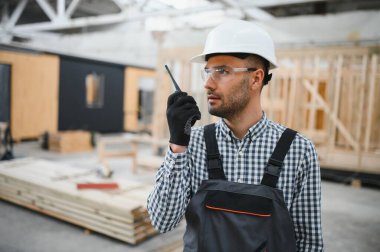 Bir mühendis modüler evlerin üretimini kontrol ediyor ve bir telsiz kullanıyor..