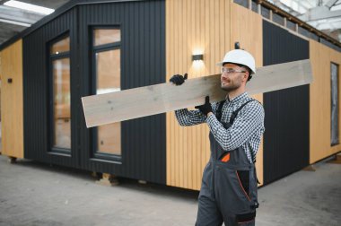 Üniformalı bir işçi ya da mühendis ahşap modüler evler için inşaat alanında çalışıyor..