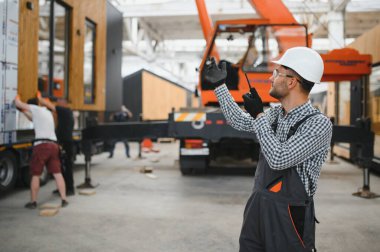 Foreman telsiz kullanarak prefabrik modüler bir evi kamyondan kamyona yüklüyor..