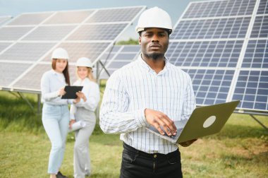 Afrikalı Amerikalı teknisyen güneş panellerinin bakımını kontrol ediyor. Güneş istasyonundaki siyah adam mühendisi..