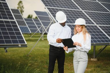 Güneş panellerinde çalışan erkek ve kadın mühendisler enerji çiftliğinde çalışıyor. Güneş enerjisi santralinde çalışan teknisyen.