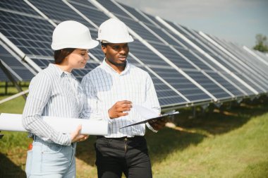 Güneş panellerinde çalışan erkek ve kadın mühendisler enerji çiftliğinde çalışıyor. Güneş enerjisi santralinde çalışan teknisyen.