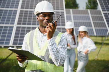Güneş panellerinde çalışan erkek ve kadın mühendisler enerji çiftliğinde çalışıyor. Güneş enerjisi santralinde çalışan teknisyen.