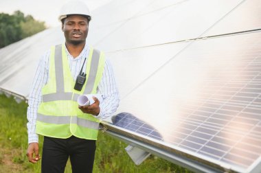 Güvenlik kaskı ve üniforma takan Afro-Amerikan elektrik mühendisinin portresi güneş panelleri kuruyor..