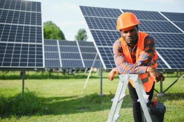 Güvenlik kaskı ve üniforma takan Afro-Amerikan elektrik mühendisinin portresi güneş panelleri kuruyor..