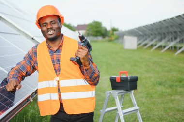 Güvenlik kaskı ve üniforma takan Afro-Amerikan elektrik mühendisinin portresi güneş panelleri kuruyor..