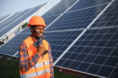 Güvenlik kaskı ve üniforma takan Afro-Amerikan elektrik mühendisinin portresi güneş panelleri kuruyor..