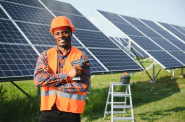 Güneş panellerinde tornavidayla güvenlik kaskı takan Afrikalı Amerikalı bir adam. İstasyonda servis çalışması yaparken araçları kullanan yetkili teknisyen.