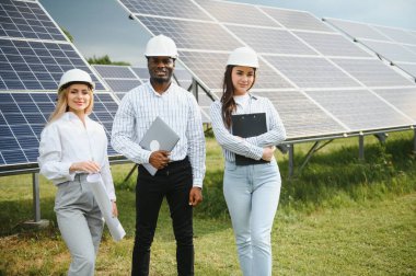 Güneş panellerinde çalışan erkek ve kadın mühendisler enerji çiftliğinde çalışıyor. Güneş enerjisi santralinde çalışan teknisyen.