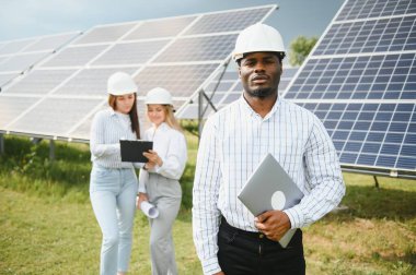 Afrikalı Amerikalı teknisyen güneş panellerinin bakımını kontrol ediyor. Güneş istasyonundaki siyah adam mühendisi..