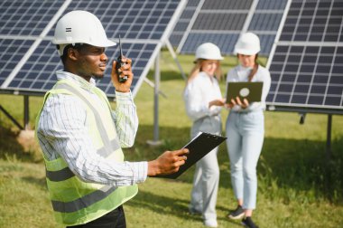 Güneş panellerinde çalışan erkek ve kadın mühendisler enerji çiftliğinde çalışıyor. Güneş enerjisi santralinde çalışan teknisyen.