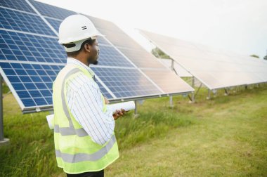Güvenlik kaskı ve üniforma takan Afro-Amerikan elektrik mühendisinin portresi güneş panelleri kuruyor..