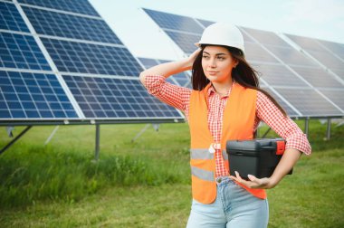 Portrait of electrician engineer in safety helmet and uniform using laptop checking solar panels. Female technician at solar station.