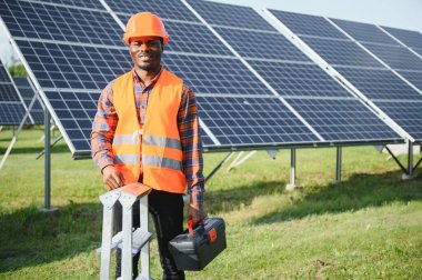Güvenlik kaskı ve üniforma takan Afro-Amerikan elektrik mühendisinin portresi güneş panelleri kuruyor..