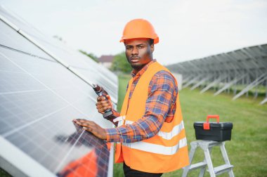 Güvenlik kaskı ve üniforma takan Afro-Amerikan elektrik mühendisinin portresi güneş panelleri kuruyor..
