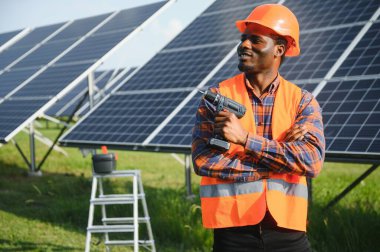 Güneş panellerinde tornavidayla güvenlik kaskı takan Afrikalı Amerikalı bir adam. İstasyonda servis çalışması yaparken araçları kullanan yetkili teknisyen.