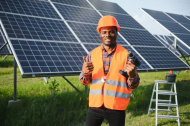 Güvenlik kaskı ve üniforma takan Afro-Amerikan elektrik mühendisinin portresi güneş panelleri kuruyor..