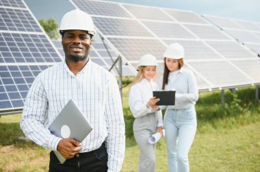 Güneş panellerinde çalışan erkek ve kadın mühendisler enerji çiftliğinde çalışıyor. Güneş enerjisi santralinde çalışan teknisyen.