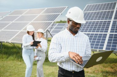Güneş panellerinde çalışan erkek ve kadın mühendisler enerji çiftliğinde çalışıyor. Güneş enerjisi santralinde çalışan teknisyen.