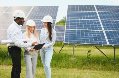 Çok ırklı insanlar dışarıda dururken yeşil enerji hakkında konuşuyorlar. Müfettişler ve ustabaşı ellerinde tablet, pano ve çizimler tutuyorlar. Güneş panelleri etrafına dizilmiş.