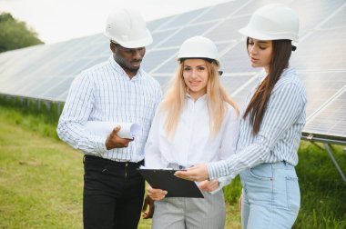 Çok ırklı insanlar dışarıda dururken yeşil enerji hakkında konuşuyorlar. Müfettişler ve ustabaşı ellerinde tablet, pano ve çizimler tutuyorlar. Güneş panelleri etrafına dizilmiş.