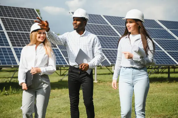 stock image Portrait of engineers standing outside near solar panels. Three workers: one woman and two men in special uniform look at camera and smiling.