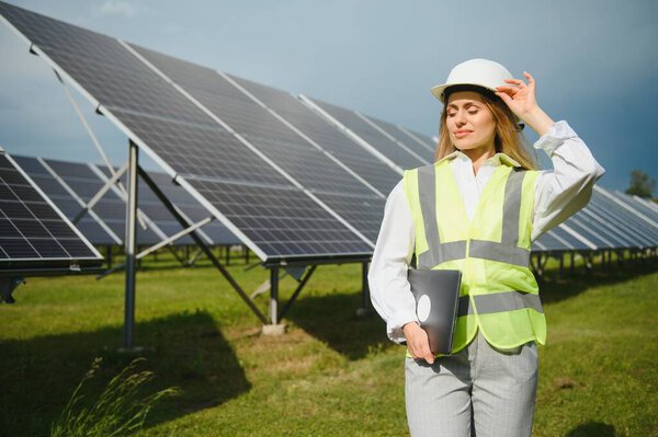 Портрет молодой женщины-инженера, стоящей возле солнечных панелей. Красивая женщина-профессионал в белом шлеме улыбается в камеру.