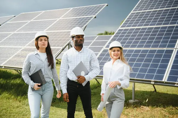 stock image Portrait of engineers standing outside near solar panels. Three workers: one woman and two men in special uniform look at camera and smiling.