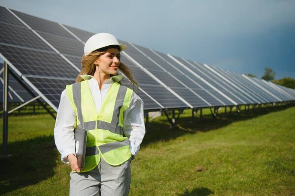 Портрет молодой женщины-инженера, стоящей возле солнечных панелей. Красивая женщина-профессионал в белом шлеме улыбается в камеру.