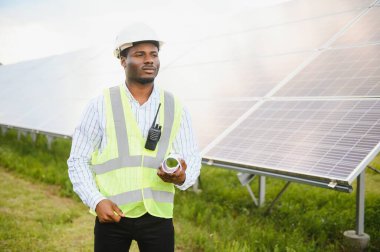 Güvenlik kaskı ve üniforma takan Afro-Amerikan elektrik mühendisinin portresi güneş panelleri kuruyor..