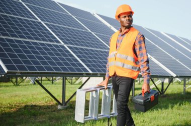 Güvenlik kaskı ve üniforma takan Afro-Amerikan elektrik mühendisinin portresi güneş panelleri kuruyor..
