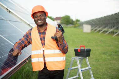 Güneş panellerinde tornavidayla güvenlik kaskı takan Afrikalı Amerikalı bir adam. İstasyonda servis çalışması yaparken araçları kullanan yetkili teknisyen.