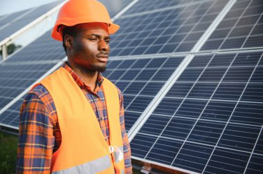 Güneş panellerinde tornavidayla güvenlik kaskı takan Afrikalı Amerikalı bir adam. İstasyonda servis çalışması yaparken araçları kullanan yetkili teknisyen.