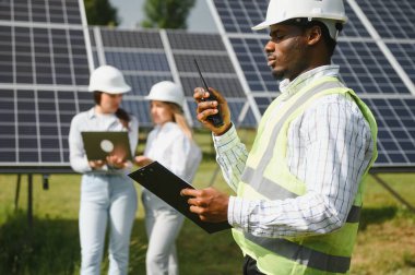 Güneş panellerinde çalışan erkek ve kadın mühendisler enerji çiftliğinde çalışıyor. Güneş enerjisi santralinde çalışan teknisyen.