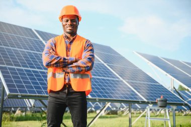 Güneş panellerinde tornavidayla güvenlik kaskı takan Afrikalı Amerikalı bir adam. İstasyonda servis çalışması yaparken araçları kullanan yetkili teknisyen.